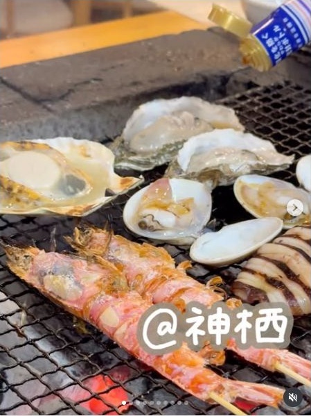 海鮮に醤油をたらして炭火で焼く場面